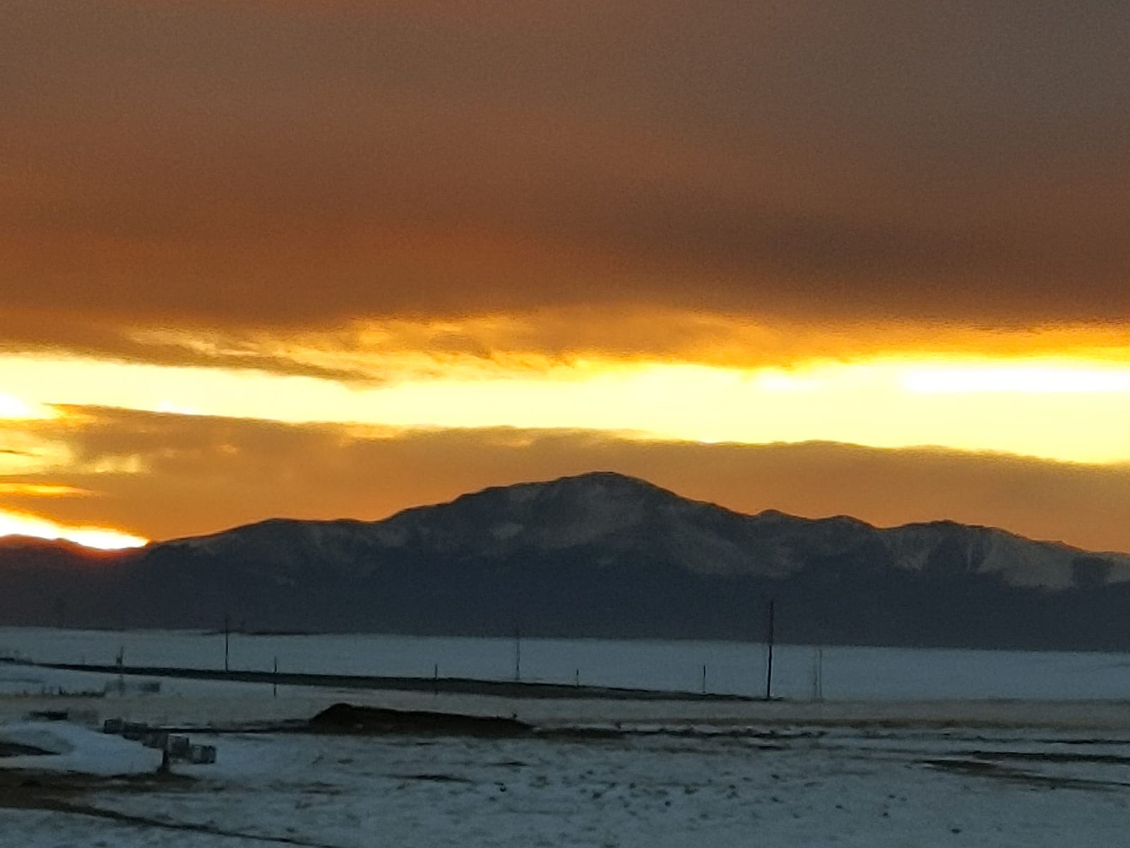 receding storm clouds allow the setting sun in west to glow golden above Pikes Peak, while snow lays on our pasture.